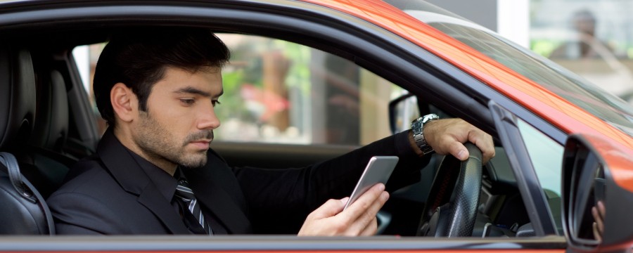 Mann mit Smartphone in rotem Auto.