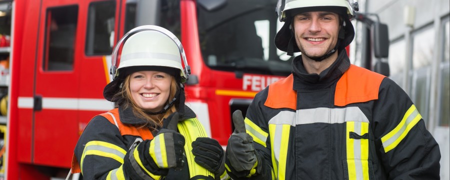 Feuerwehrfrau und Feuerewehrmann vor Feuerwehreinsatzwagen