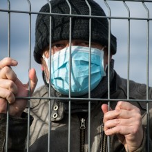 Ein Mann mit Maske hinter einem Zaun.