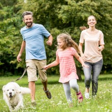 Glücklich Familie läuft mit Hund durch den Garten