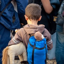 Flüchtlingskind mit Rucksack und Stofftier