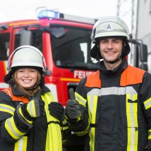 Feuerwehrfrau und Feuerewehrmann vor Feuerwehreinsatzwagen